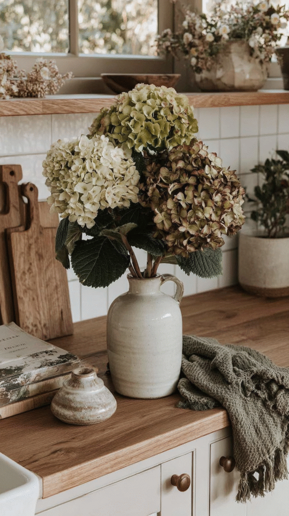 Vase with hydrangeas on wooden kitchen counter, surrounded by rustic decor and greenery.
