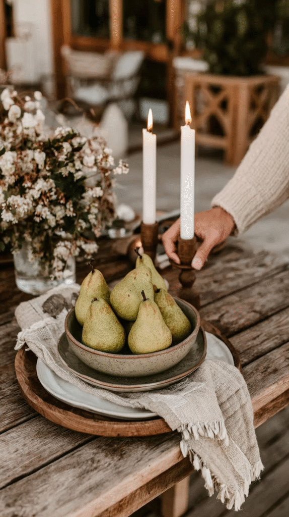 Rustic table setting with fresh pears, lit candles, and flowers, creating a cozy, inviting atmosphere outdoors.